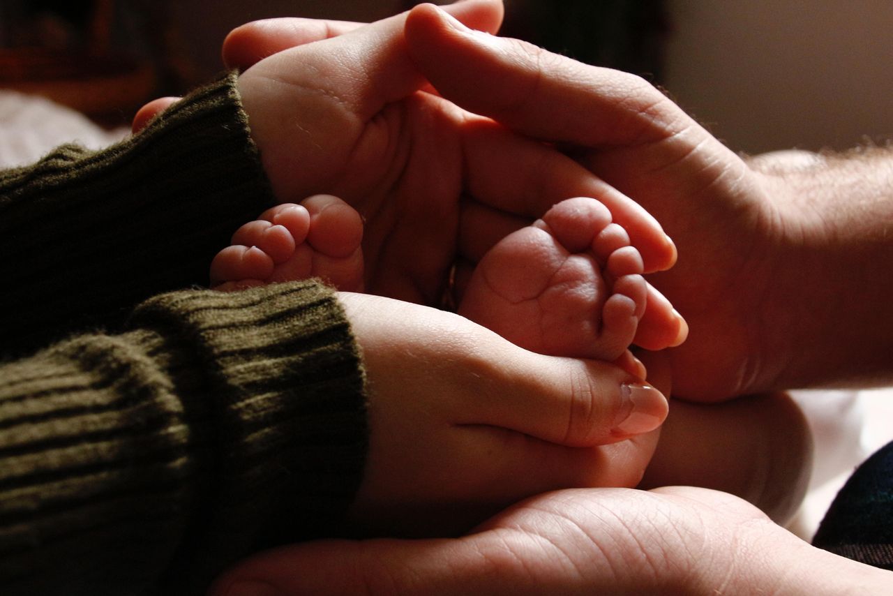 services-01 Close-up of baby feet held by adult hands, symbolizing family love and care.