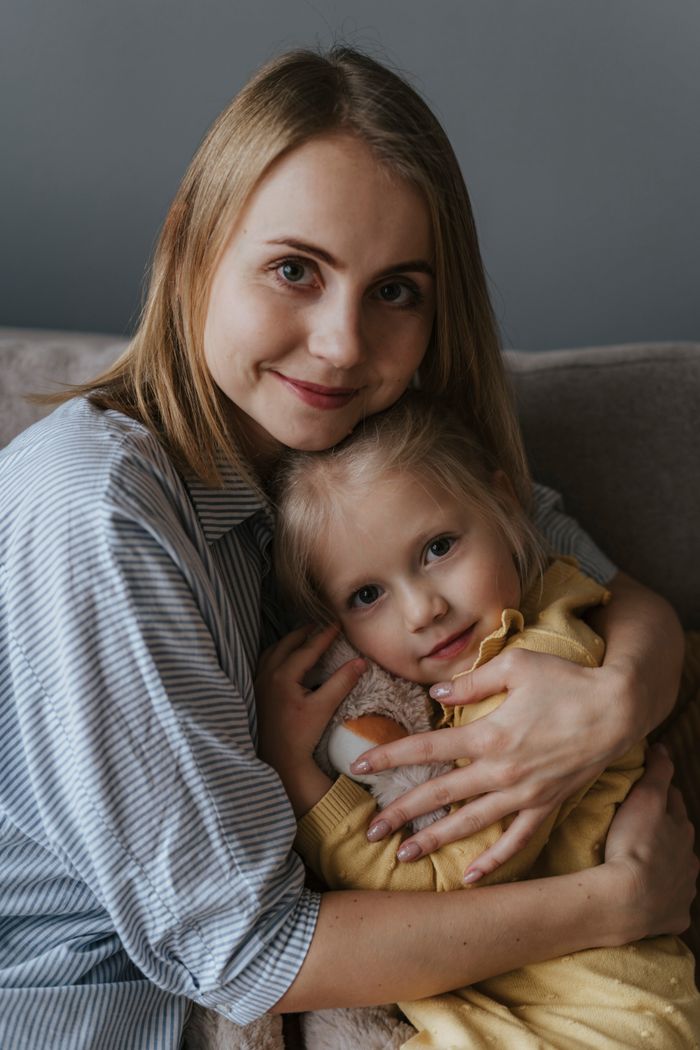 about-01 A loving mother embraces her daughter indoors, creating a warm and joyful portrait.