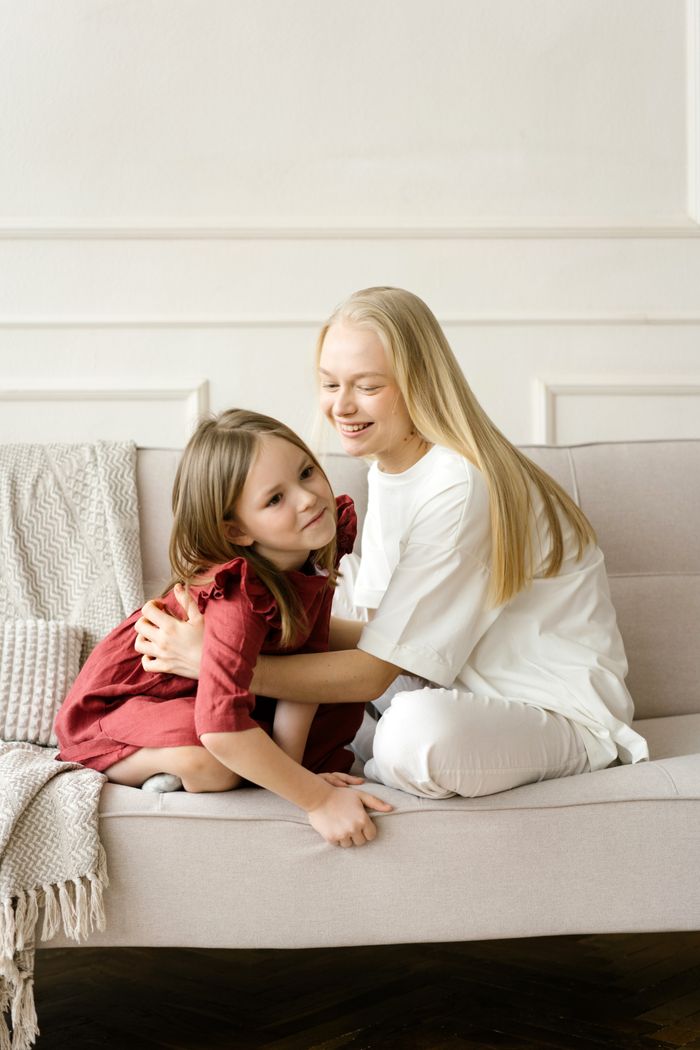 gallery-3 Warm indoor scene of a mother embracing her daughter on a sofa, capturing love and connection.