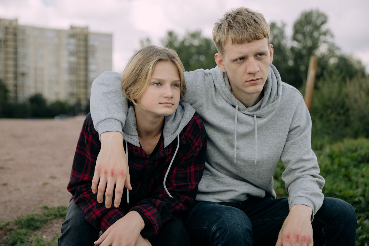 gallery-6 Two siblings in casual hoodies sit together outdoors, conveying a relaxed and thoughtful moment.