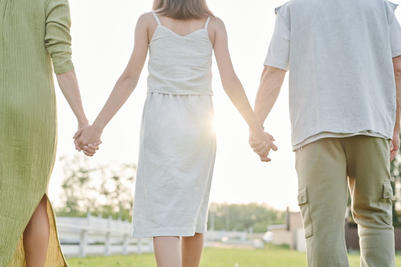 why-choose-us Three people holding hands, walking outdoors in bright sunlight, symbolizing togetherness.
