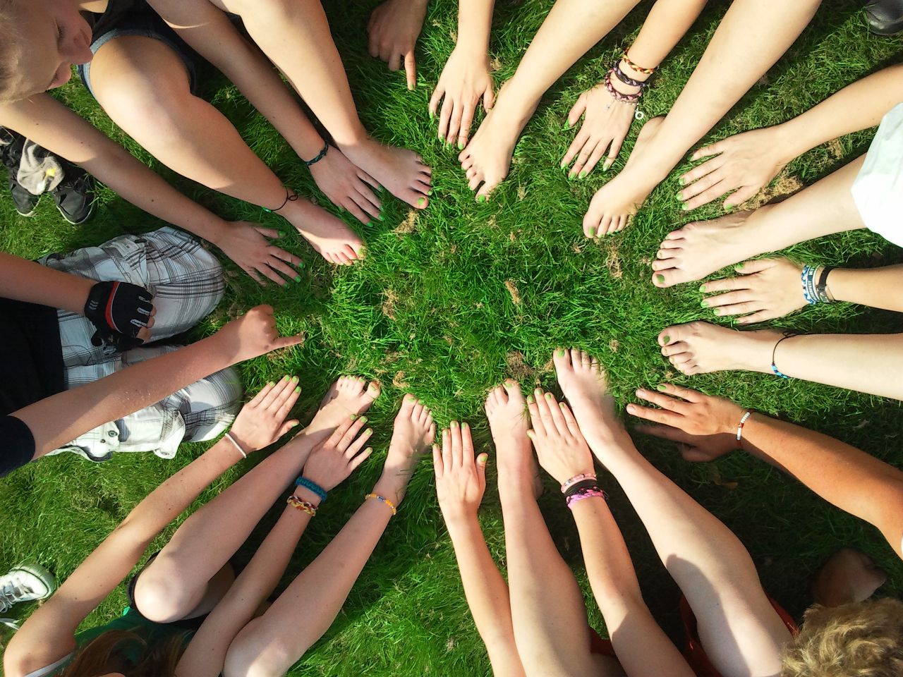 gallery-5 Group of friends forming a circle with their hands and feet on grass, symbolizing unity and friendship.